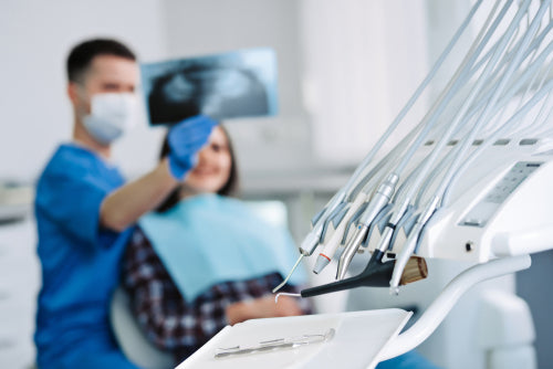 Dental instruments with dentist and patient looking at x-ray on background.