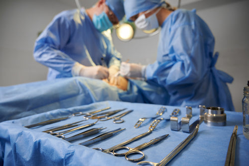 Plastic surgery instruments on surgical table with medical team and patient on blurred background. Doctor and assistant performing aesthetic surgery.